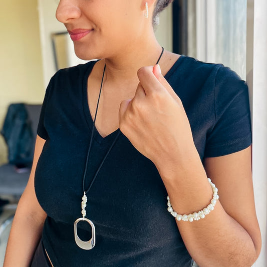Woman wearing a necklace and bracelet, pointing to her jewelry.