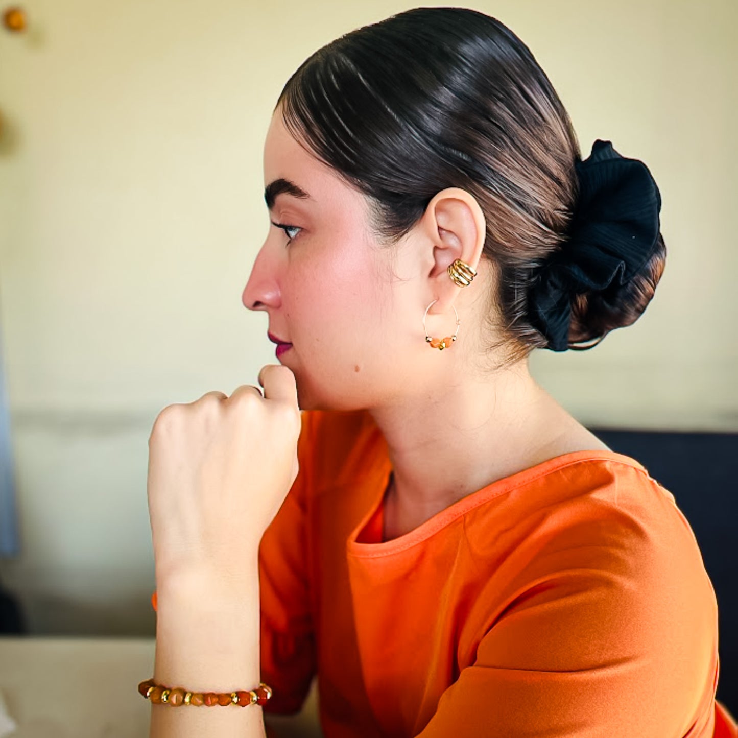 Woman with an elegant bun hairstyle wearing gold and orange agate earrings and bracelet