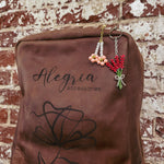 A brown leather bag with the Alegria Accessories logo displaying two flower bag charms including peach blossoms and a red flower bouquet