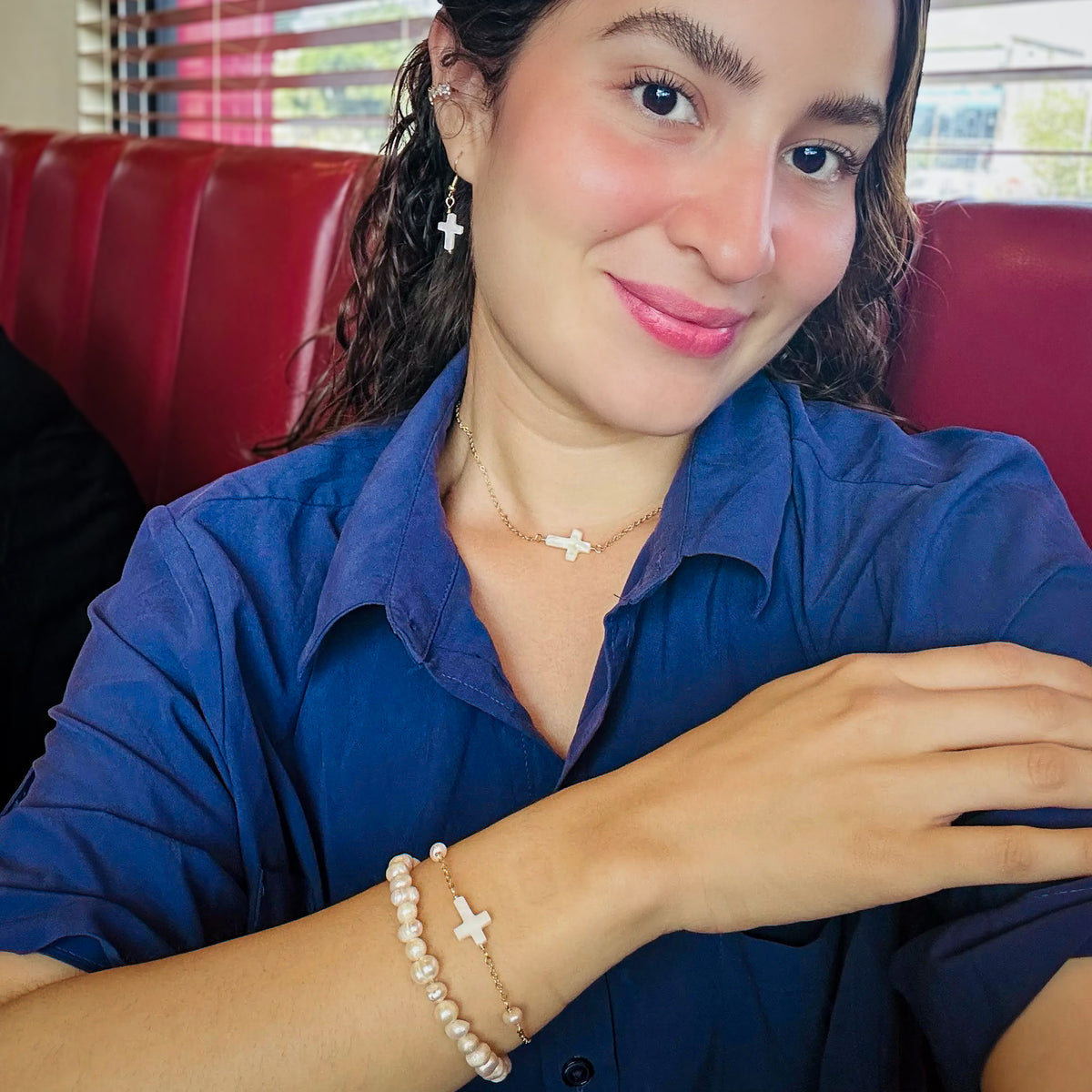 Woman modeling gold and mother of pearl cross jewelry set with dangle earrings, short pendant necklace, and two-piece bracelet set with beaded stretch and chain bracelets