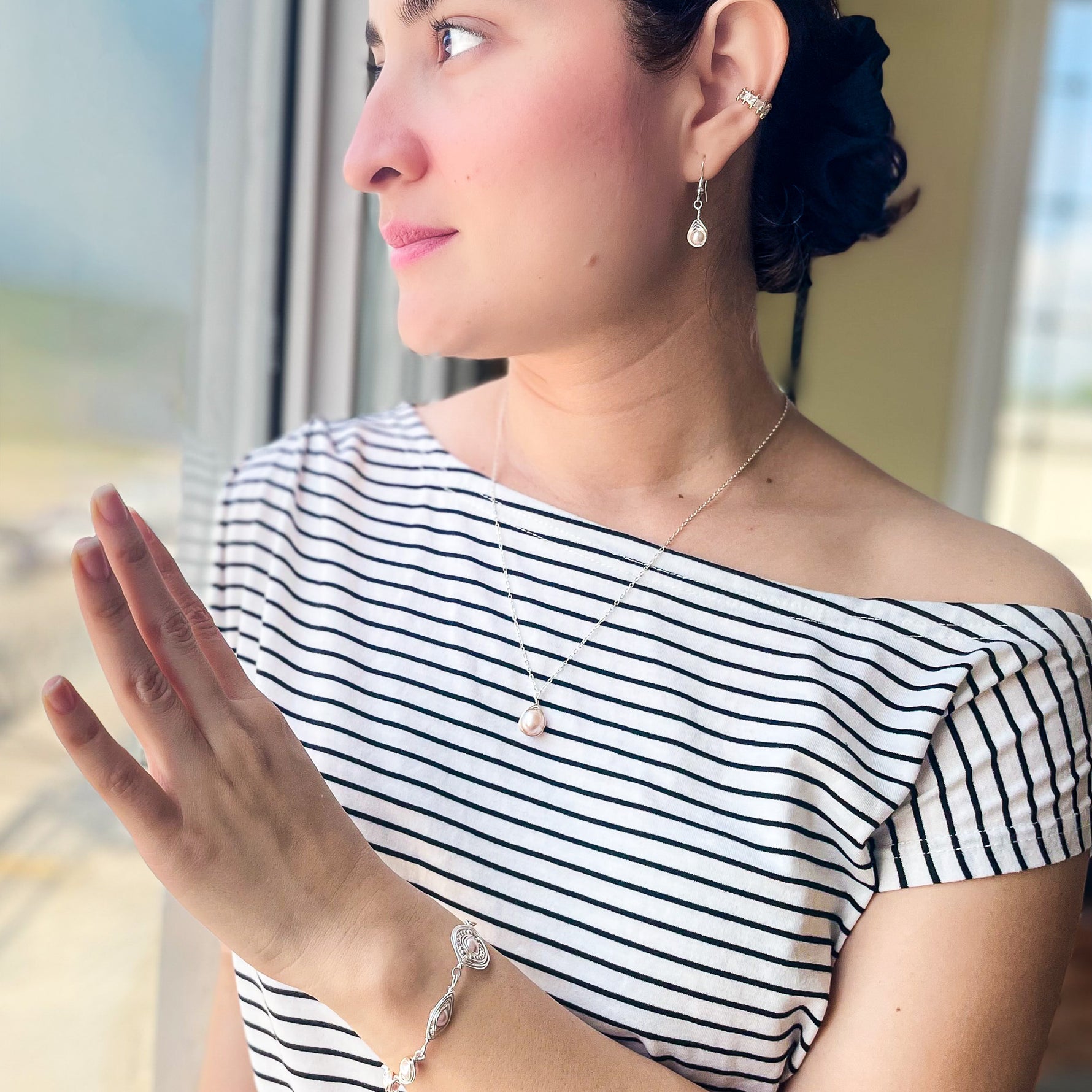 Woman wearing a black and white striped top with jewelry, looking out a window.