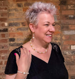 Woman modeling white moonstone, mother of pearl, and gold beaded cross jewelry with stretch bracelet and multi-strand necklace