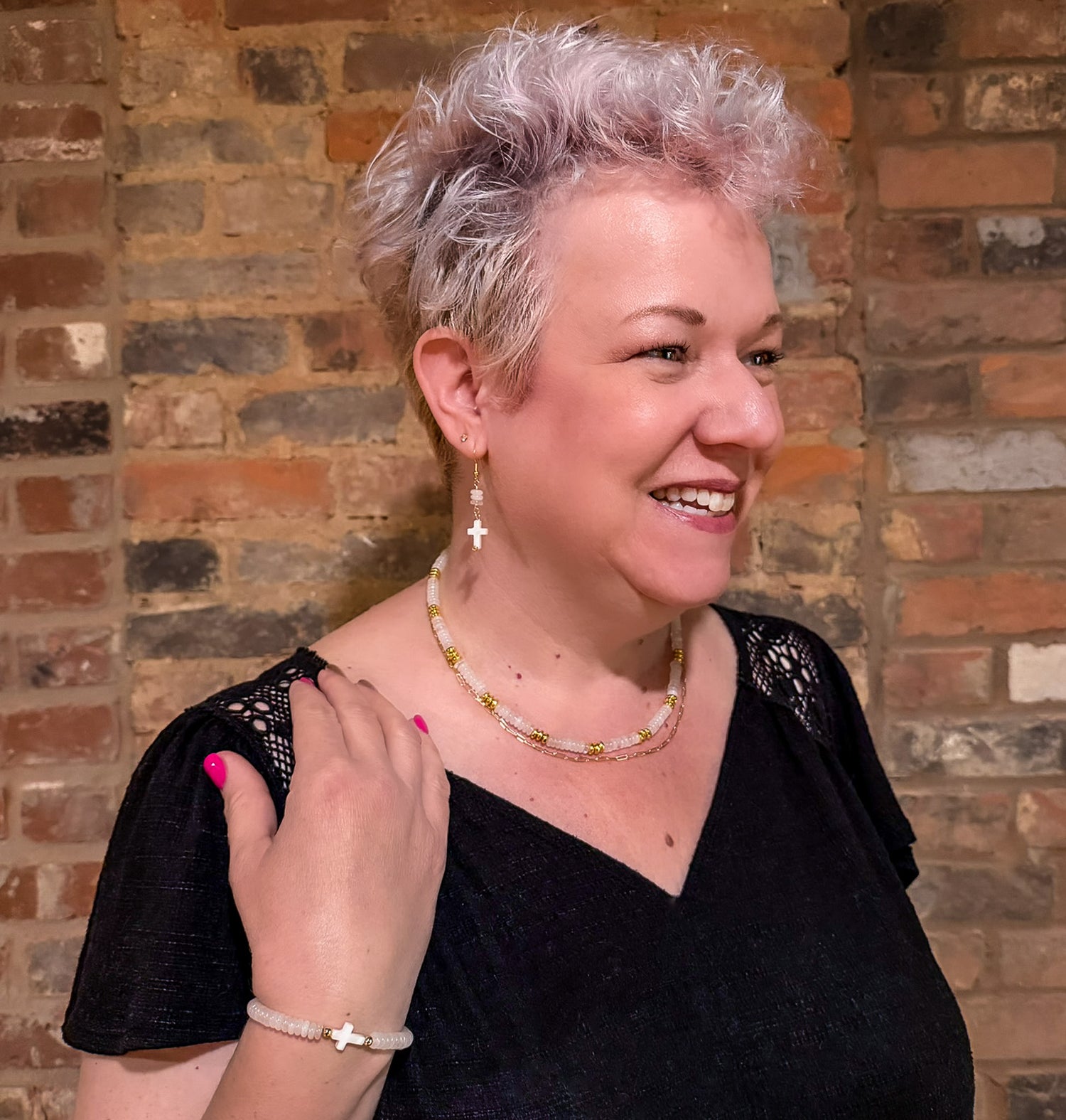 Woman modeling white moonstone, mother of pearl, and gold beaded cross jewelry with stretch bracelet and multi-strand necklace