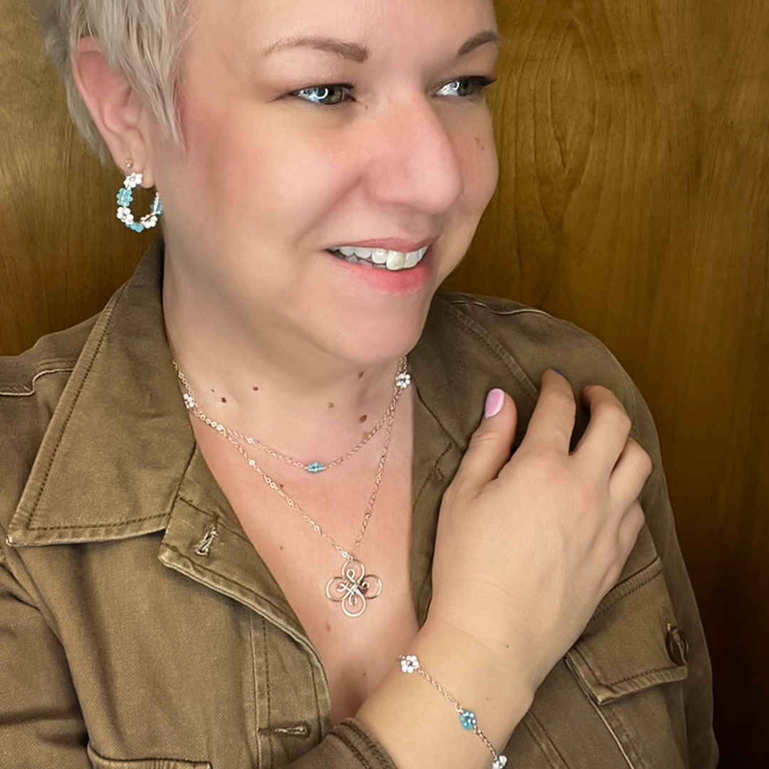 Woman modeling blue and white flower and silver jewelry including hoop earrings and multi-strand necklace