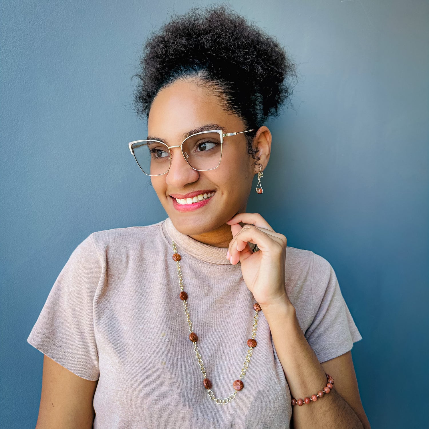 Woman modeling gold and goldstone jewelry set including intricate flower dangle earrings, beaded adjustable cord bracelet, and long chain and station bead necklace