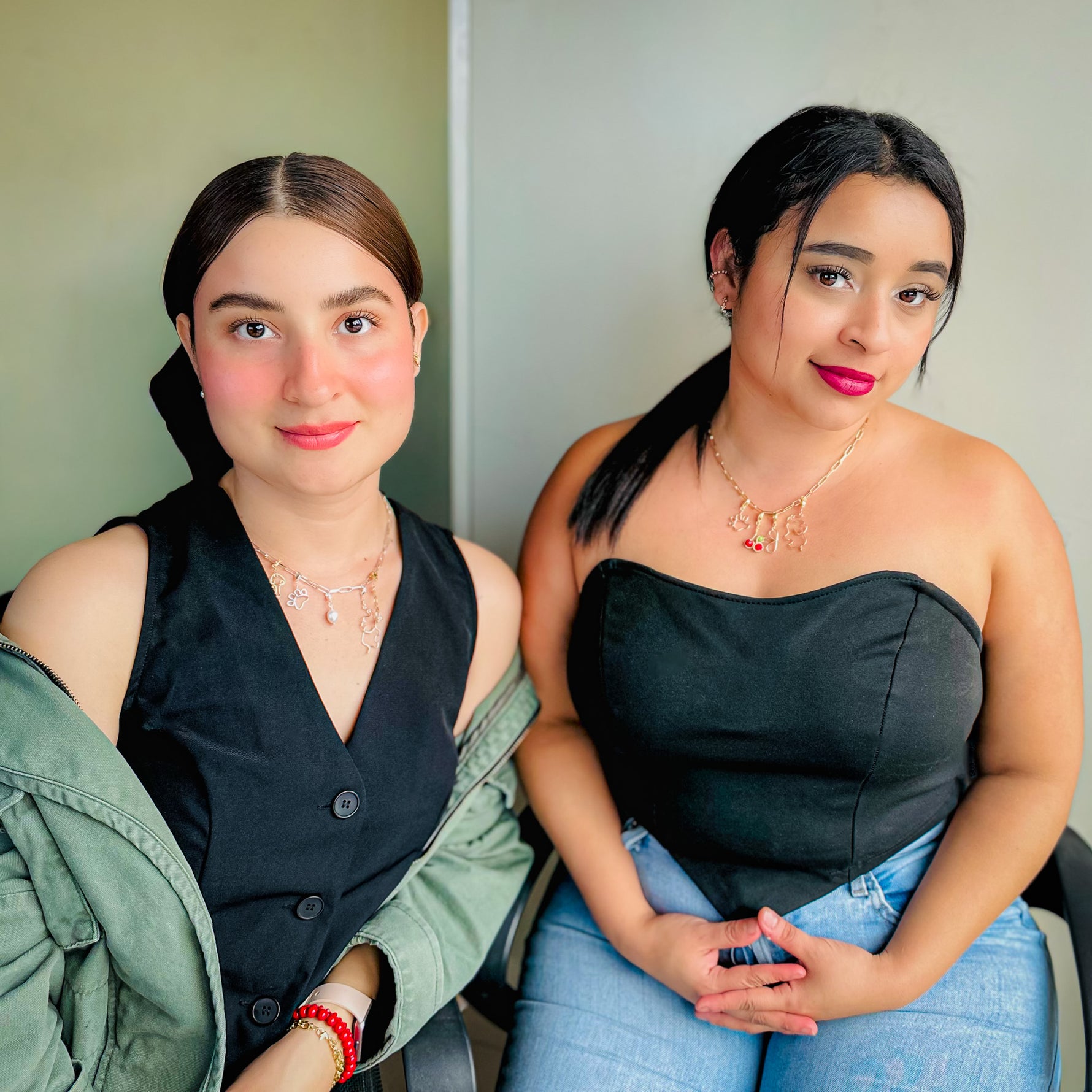 Two women sitting wearing gold charm necklaces