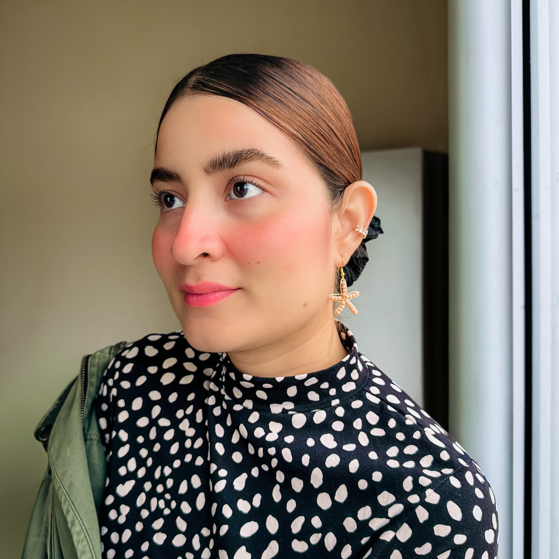 Woman modeling gold starfish dangle earrings with peach crystal design