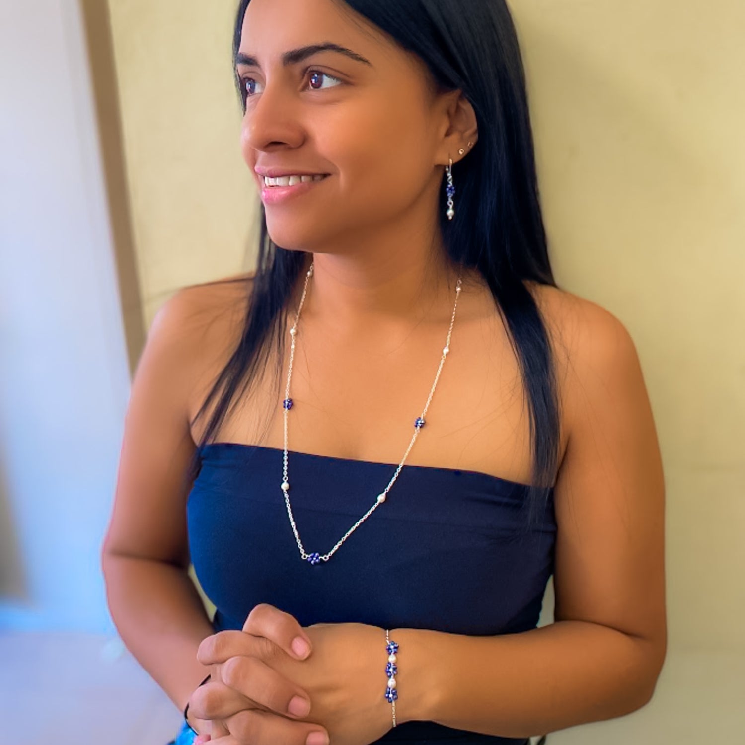 Woman modeling blue crystal and freshwater pearl jewelry set including dangle earrings, long station necklace, and chain bracelet