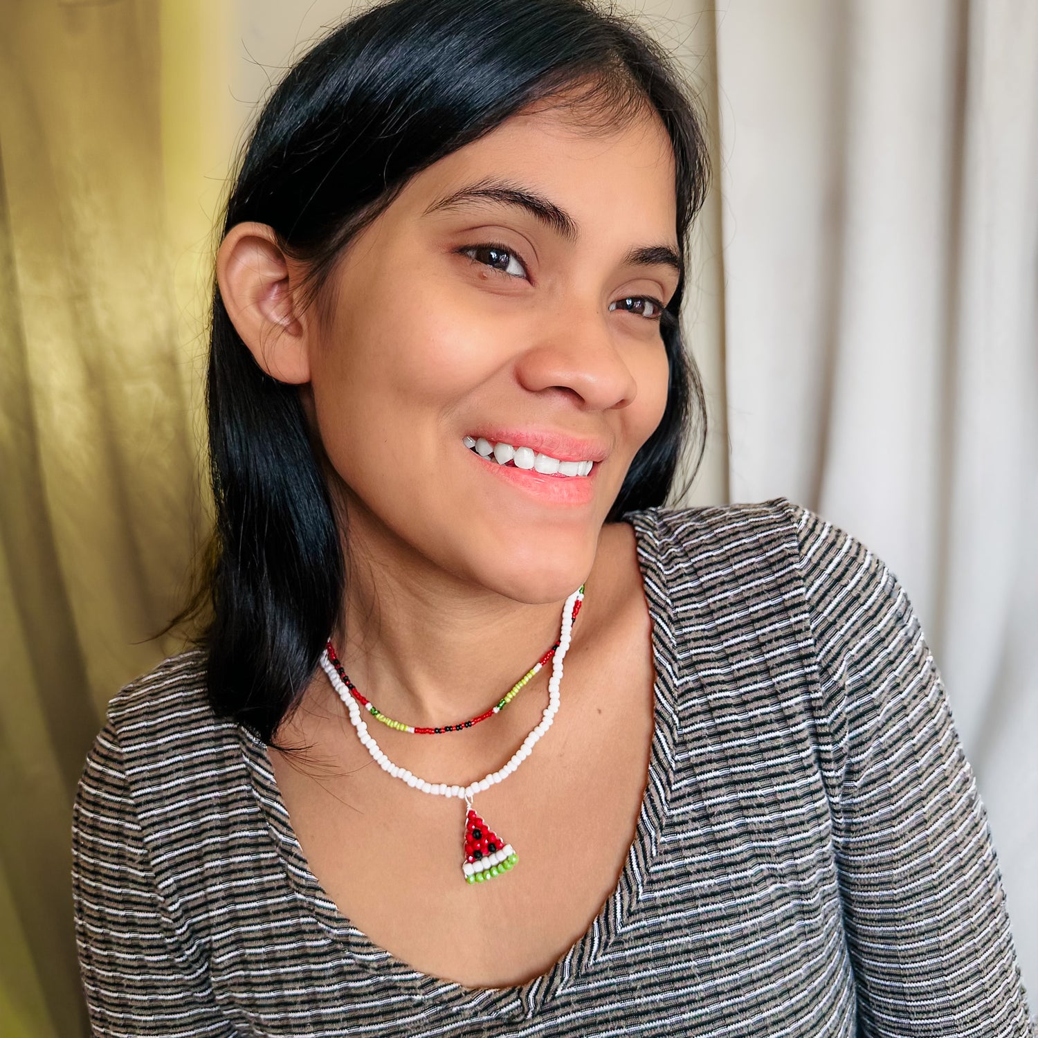 Woman modeling short, multi-strand beaded necklace including red, green, and black watermelon pattern strand and white strand with watermelon pendant